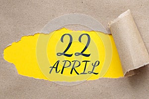 April 22. 22th day of the month, calendar date.Hole in paper with edges torn off. Yellow background is visible through