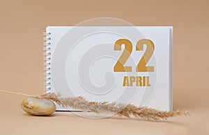 April 22. 22th day of the month, calendar date.White blank sheet of notepad, stones, dry sprig of grass, on beige background.