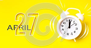 April 27th. Day 27 of month, Calendar date. White alarm clock  with calendar day on yellow background. Minimalistic concept of