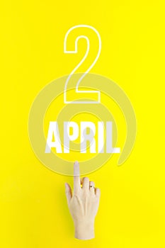 April 2nd. Day 2 of month, Calendar date.Hand finger pointing at a calendar date on yellow background.Spring month, day of the