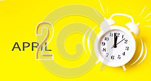 April 2nd. Day 2 of month, Calendar date. White alarm clock  with calendar day on yellow background. Minimalistic concept of time