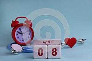 April 8st. White wooden calendar blocks with date, clock and stethoscope on a blue pastel background. Selective focus. health