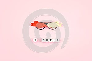 April Fools ' Day celebration. Glasses with paper fish and text 1 April on pink background. All Fools ' Day, humor, prank, joke