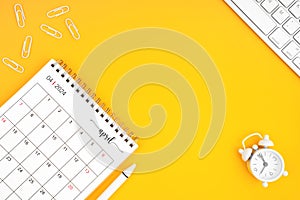 April 2024, Monthly desk calendar for 2024 year and alarm clock with paper clips on yellow color background