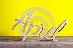 April - wooden carved word on yellow background. Spring time, 1st of april - Easter and fools day