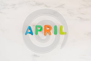 April word written with colorful letters on white marble stone background