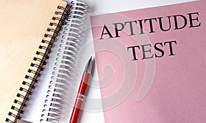 APTITUDE TEST text on pink paper with notebooks photo