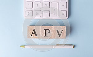 APV word on wooden block with pen and calculator on blue background