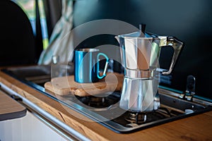 Aqua Bialetti stovetop coffee maker and mug, on a van gas cooker