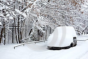 Ð¡ar is covered with fresh white snow on the background of a fence and snow-covered maples