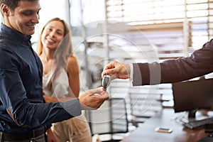 Ar salesman giving car keys to young woman sitting in car in auto dealership