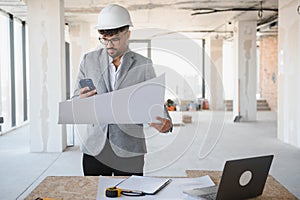 Arab Architect using smartphone and holding blueprint at construction site
