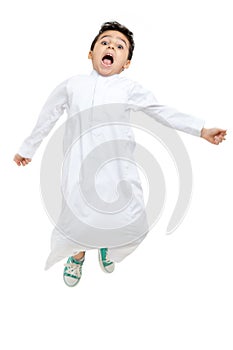 Arab boy jumping high with a big smile and open eyes, wearing white traditional Saudi Thobe and sneakers, on white isolated photo
