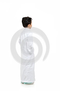 Arab boy looking at background with hand in his pockets, wearing white traditional Saudi Thobe and sneakers, raising his hands on photo