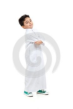 Arab boy smiling and acting cool with crossed hands, wearing white traditional Saudi Thobe and sneakers, on white isolated photo