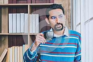 Arab businesman in casual clothes taking a break from work, standing near the window holding cup of coffee blurred black ground of