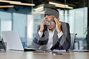 Arab businessman in glasses suffering from headache, sitting in new office working, holding his head, writhing in pain