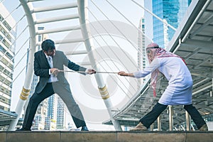 Arab businessmen and businessman playing tug of war on city