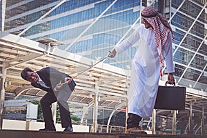 Arab businessmen and businessman playing tug of war on city back