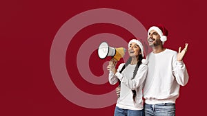 Arab Couple In Santa Hats Making Announcement With Loudspeaker Over Red Background