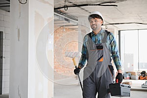 Arab engineer holding paint roller and toolbox walking on construction site