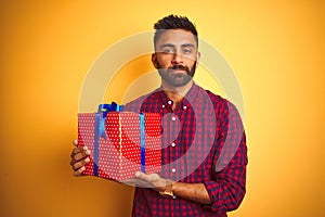 Arab indian hispanic man holding birthday gift standing over isolated yellow background with a confident expression on smart face