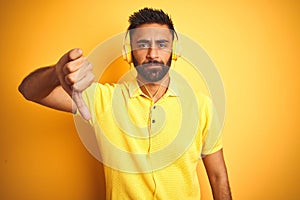 Arab indian hispanic man listening to music using headphones over isolated yellow background with angry face, negative sign