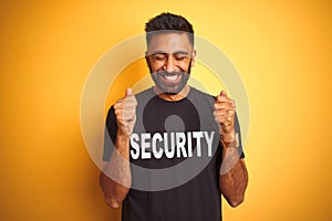 Arab indian hispanic safeguard man wearing security uniform over isolated yellow background excited for success with arms raised