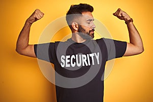 Arab indian hispanic safeguard man wearing security uniform over isolated yellow background showing arms muscles smiling proud