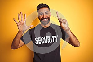 Arab indian hispanic safeguard man wearing security uniform over isolated yellow background showing and pointing up with fingers