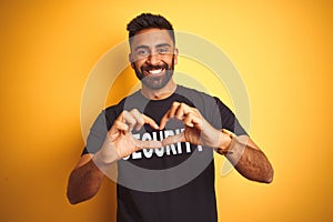 Arab indian hispanic safeguard man wearing security uniform over isolated yellow background smiling in love doing heart symbol
