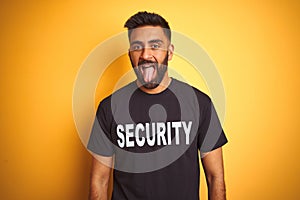 Arab indian hispanic safeguard man wearing security uniform over isolated yellow background sticking tongue out happy with funny
