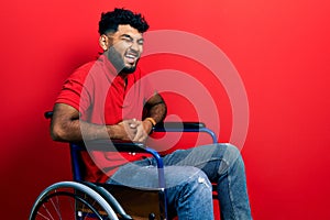 Arab man with beard sitting on wheelchair smiling and laughing hard out loud because funny crazy joke with hands on body