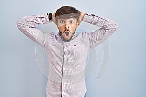 Arab man with beard standing over blue background crazy and scared with hands on head, afraid and surprised of shock with open