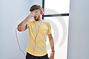Arab man with beard wearing sportswear and headphones relaxed with serious expression on face