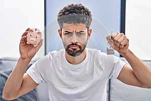 Arab man holding piggy bank and house keys depressed and worry for distress, crying angry and afraid