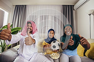 Arab man looking TV at home during a sport event with his family.