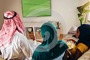 Arab man looking TV at home during a sport event with his family.