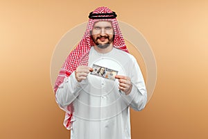 An Arab man in a national costume holds dollars in his hands on a beige background