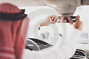 Arab man sits in a new car and adjusts the mirror.