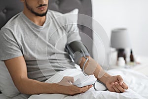 Arab Man Sitting In Bed, Checking Blood Pressure With Upper Arm Monitor