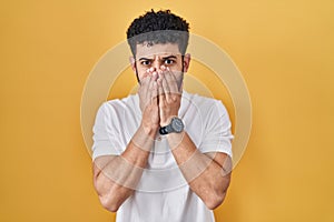 Arab man standing over yellow background shocked covering mouth with hands for mistake