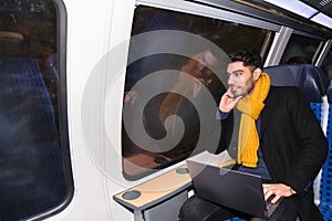 Arab man in train holds laptop and looks at camera