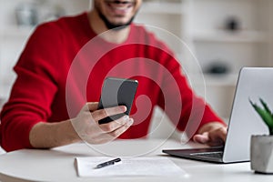 Arab Man Using Modern Mobile Phone While Sitting At Desk With Laptop