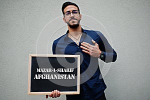 Arab man wear blue shirt and eyeglasses hold board with Mazar-i-Sharif Afghanistan inscription. Largest cities in islamic world