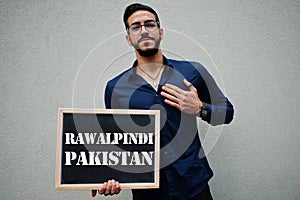 Arab man wear blue shirt and eyeglasses hold board with Rawalpindi Pakistan inscription. Largest cities in islamic world concept