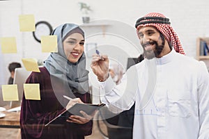 Arab man and woman working in offce. Coworkers are taking notes on glass board.