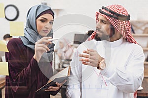 Arab man and woman working in offce. Coworkers are taking notes on glass board.
