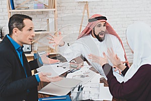 Arab man yells at wife who is sitting near table.