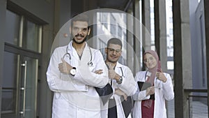 Arab medical team in white lab coats standing with folded arms in row and showing thumbs up